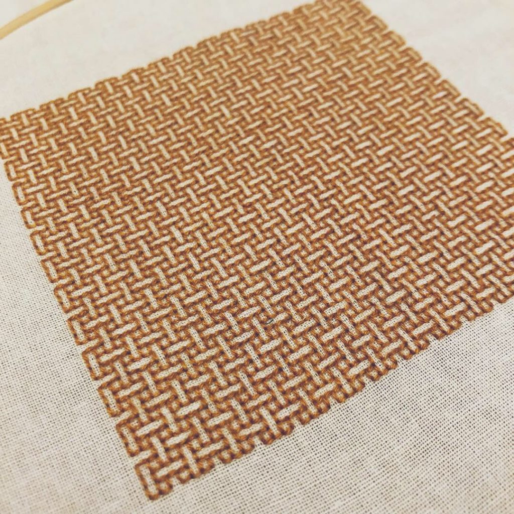 A close-up of the square of amber embroidery in a weave pattern, on white fabric